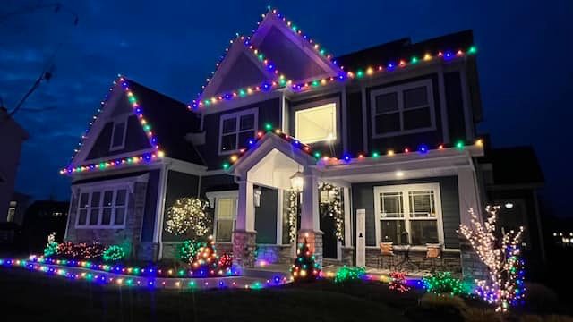 A Two Story Pittsburgh Gray Suburban Home with White Trim is Illuminated at Night by Colorful Holiday Christmas Lights.